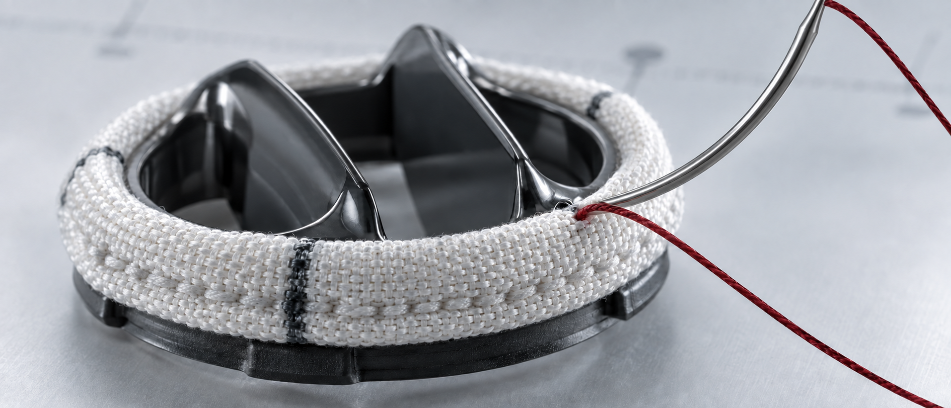 Curved surgical needle carrying red suture through the woven sewing cuff of a mechanical heart valve